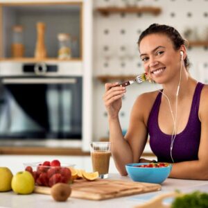 Young happy athletic woman eating fruit salad in the kitchen