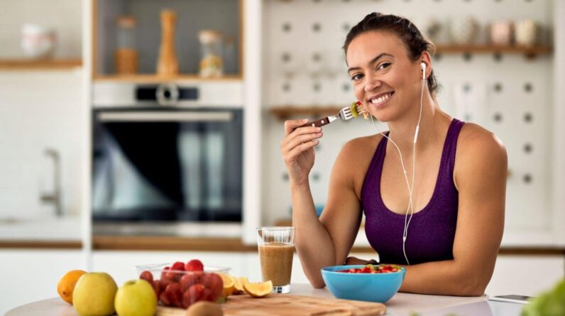 Young happy athletic woman eating fruit salad in the kitchen